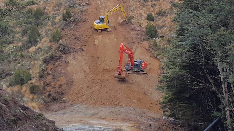 A yellow and an orange digger working on a steep dirt slope.